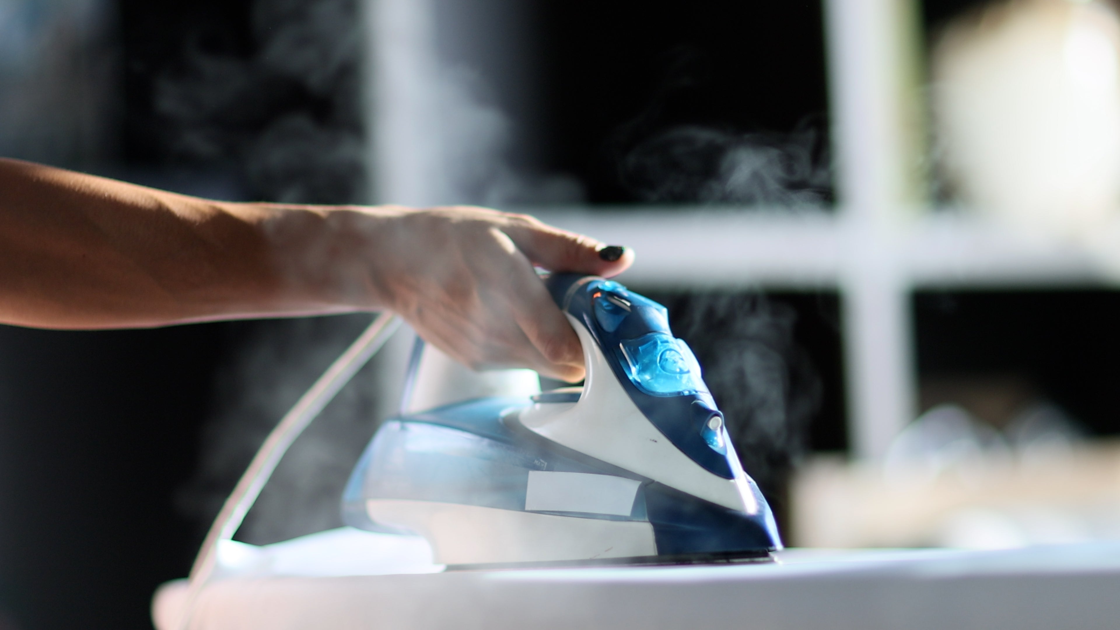 Person using a steam iron on a white surface with a blurred background