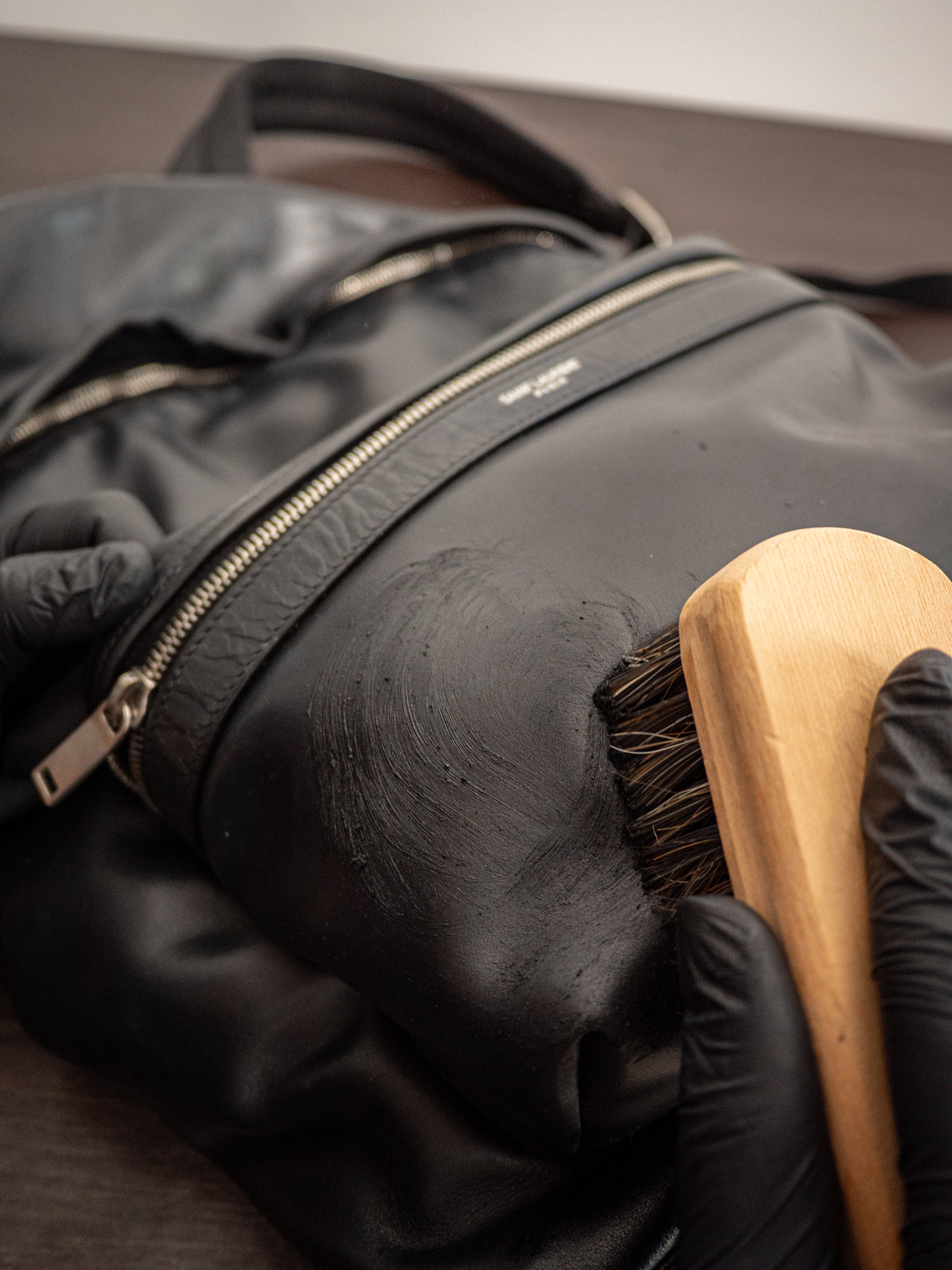 black branded leather bag being brushed during a wax treatment