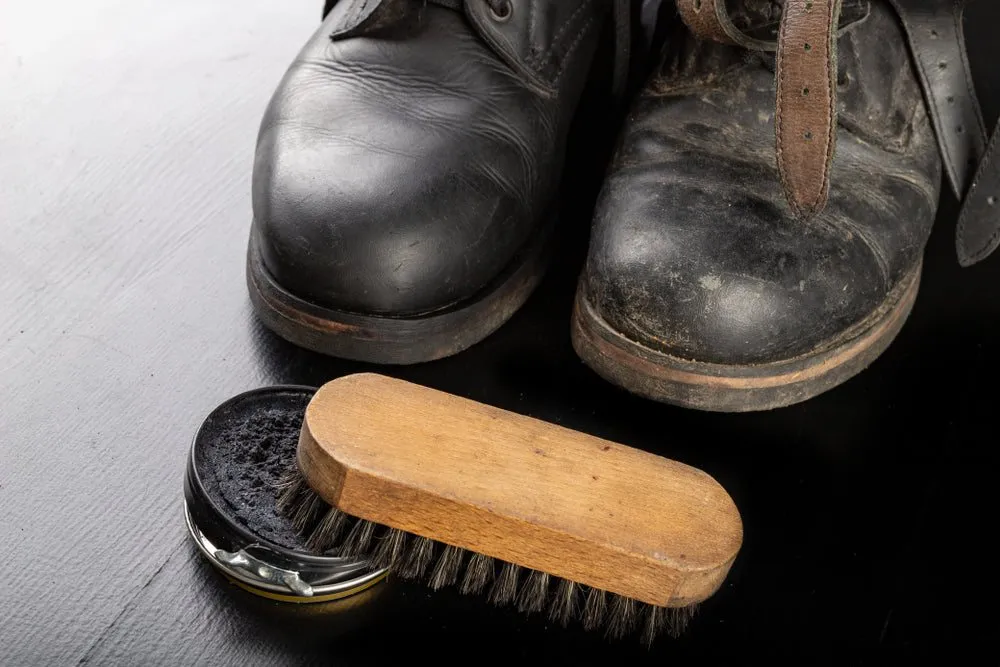 Before and after comparison of black leather shoes with wax and brush on a black table