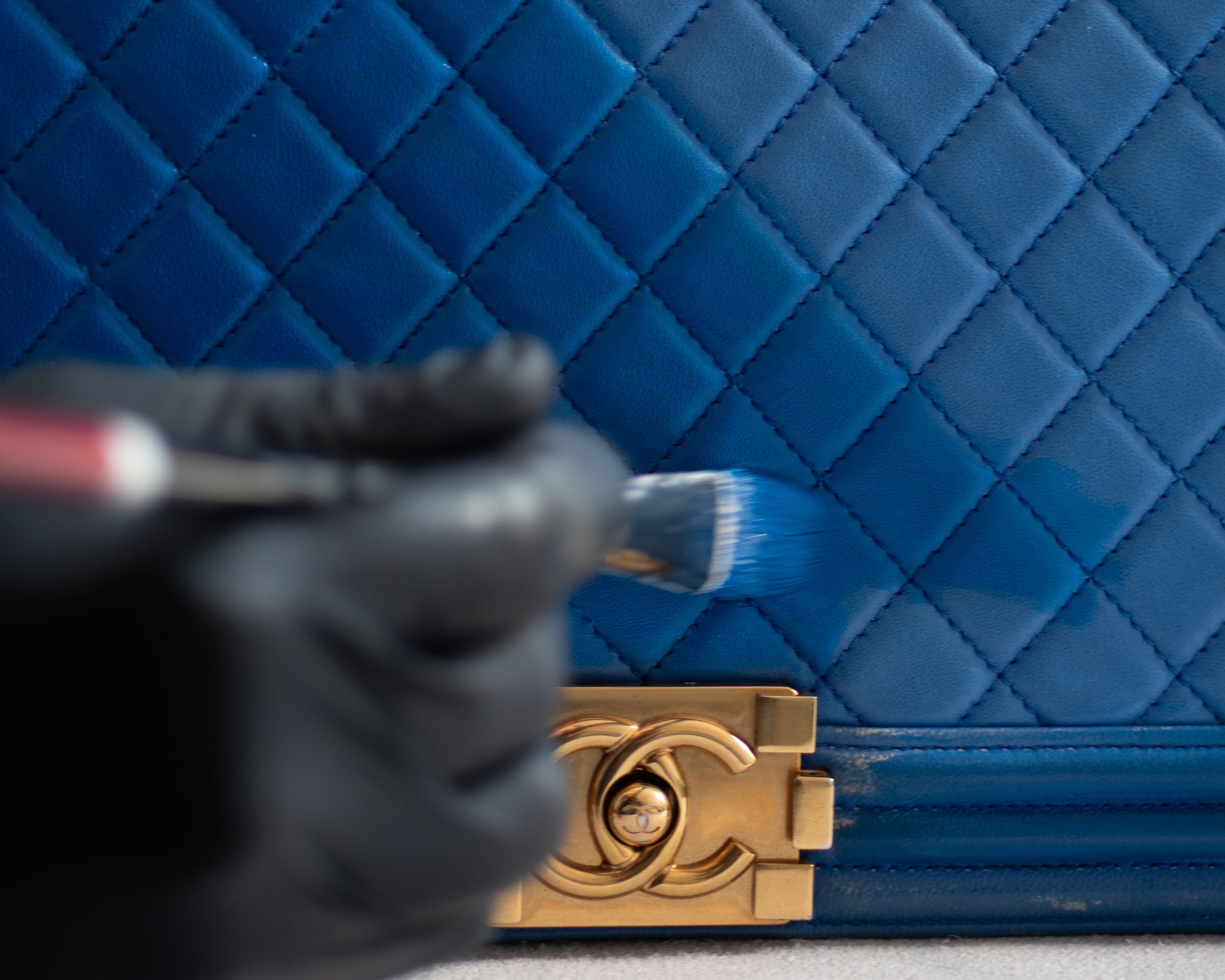 Blue quilted handbag with gold clasp on a neutral background being paint restored