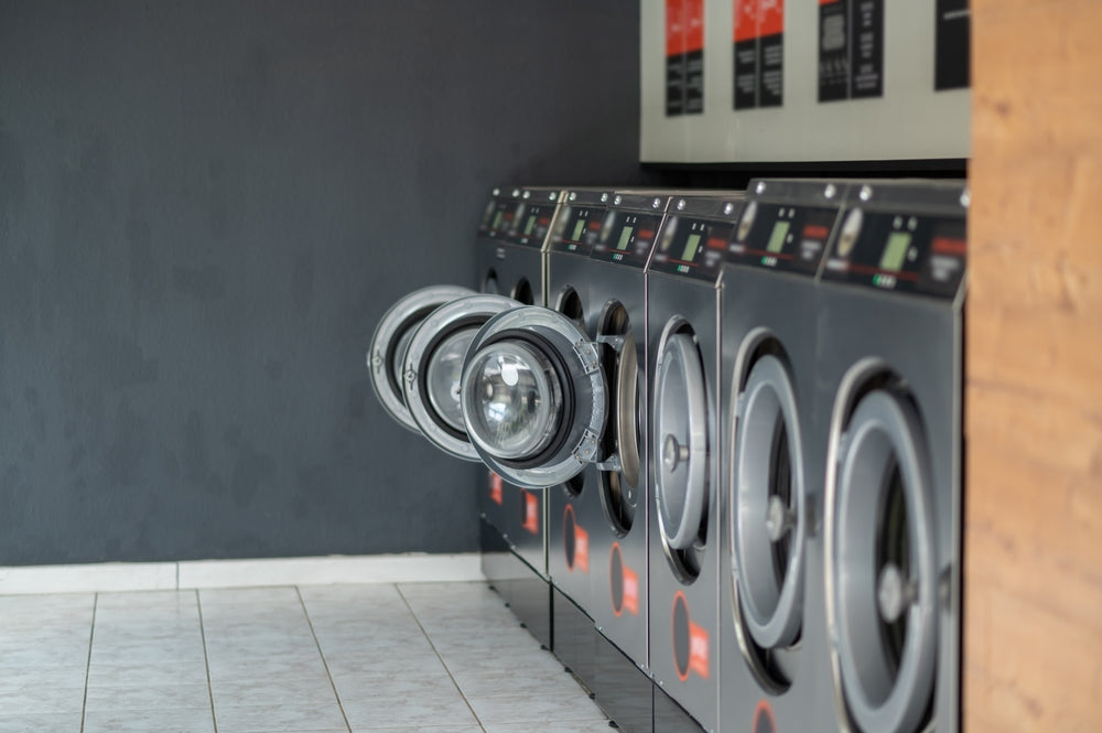 7 commercial laundry machines lined up agianst a grey wall