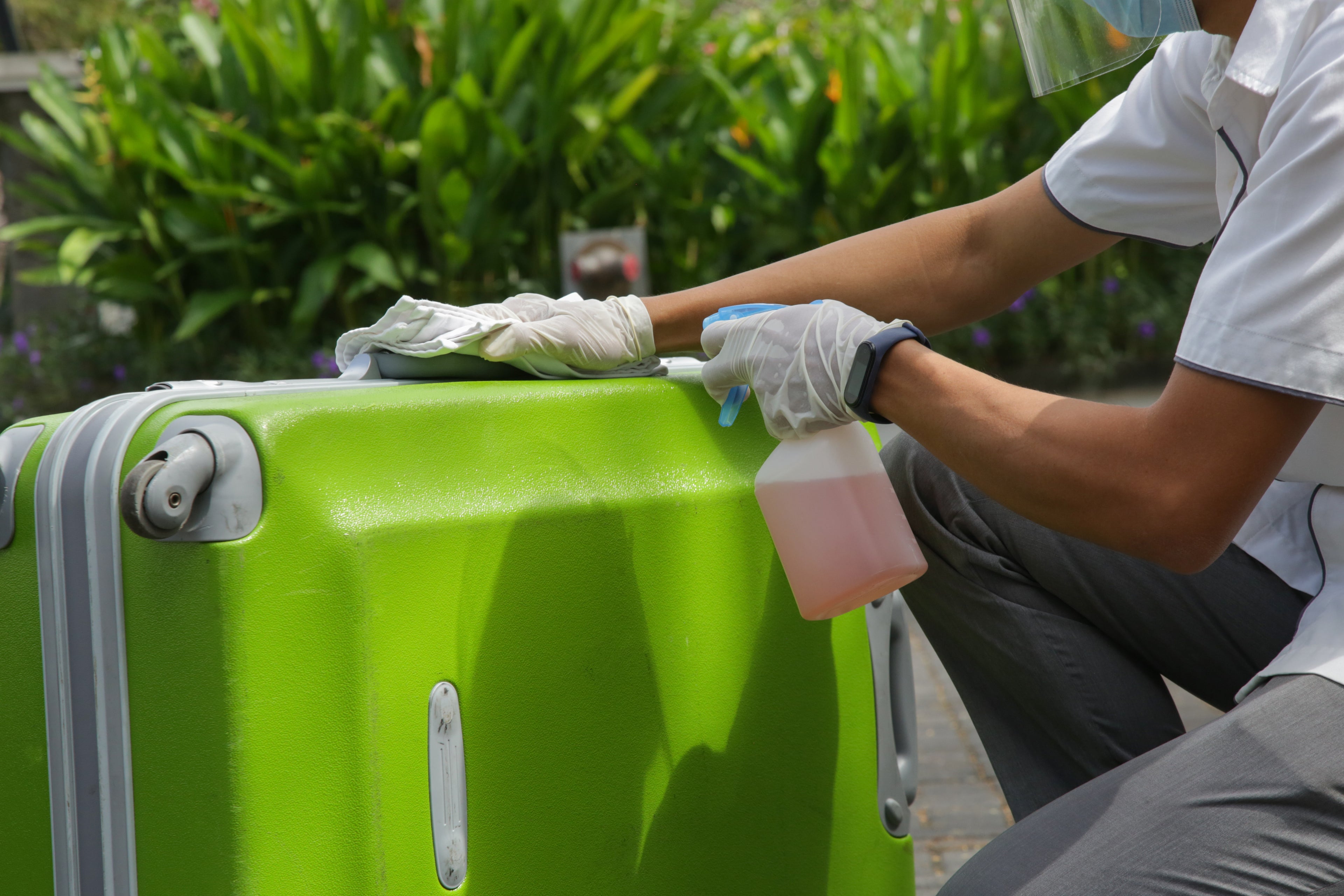 Person cleaning a green suitcase with a spray bottle outdoors