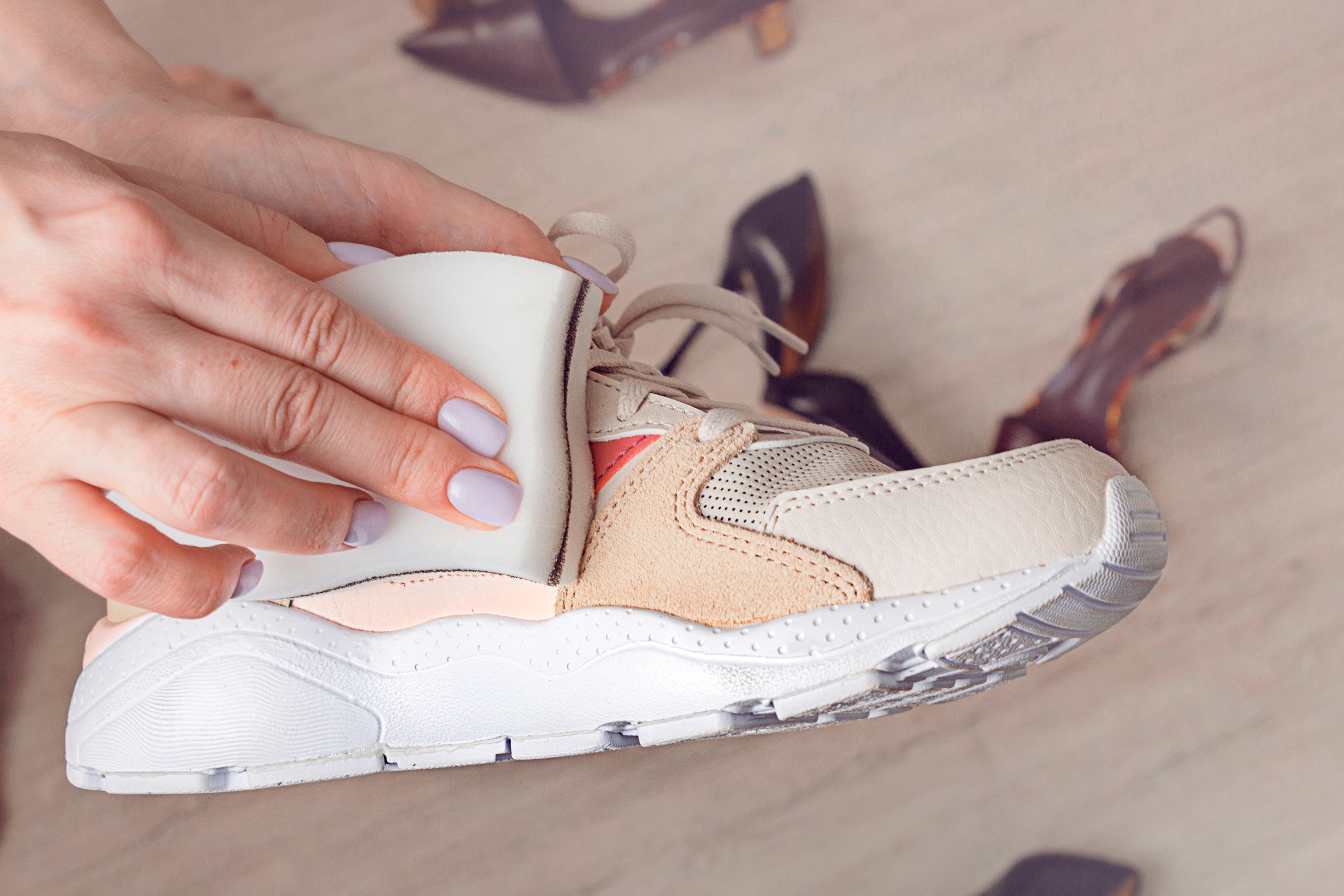 Close-up of a hand holding a white sneaker with beige accents on a light background