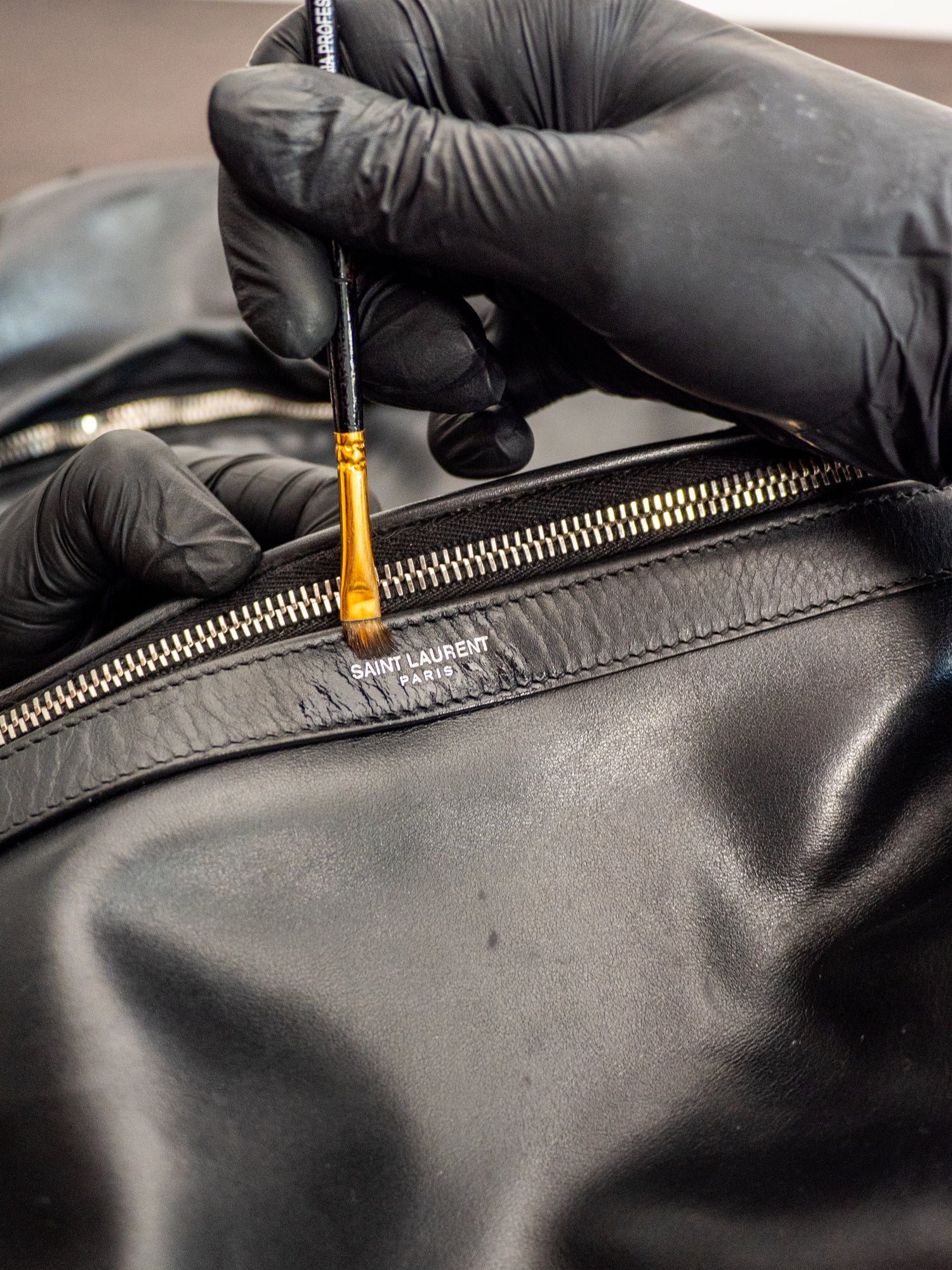 Person applying paint to a Yves Saint Laurent leather backpack using a brush.